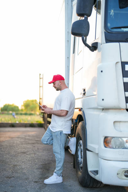 motorista homem com tablet na mão em chapéu vermelho parado perto do caminhão - semi truck driver pride white - fotografias e filmes do acervo