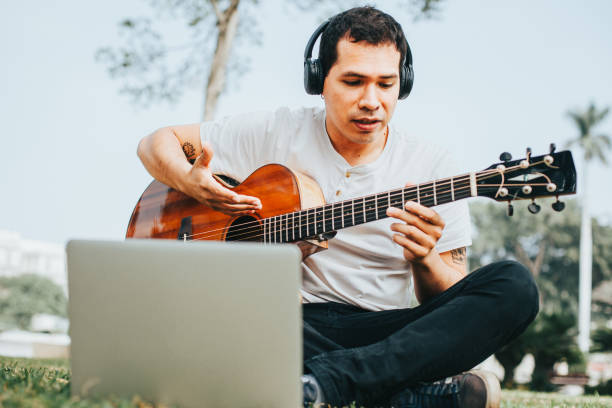 istock Young man playing guitar and teaching on a laptop in a park. 1543034110
