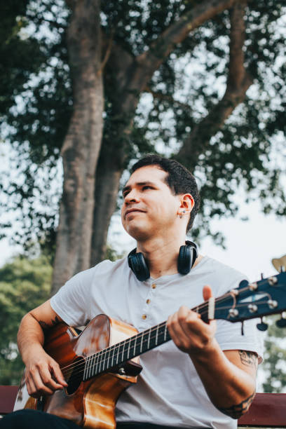 istock Man playing acoustic guitar sitting in a park. 1543043363