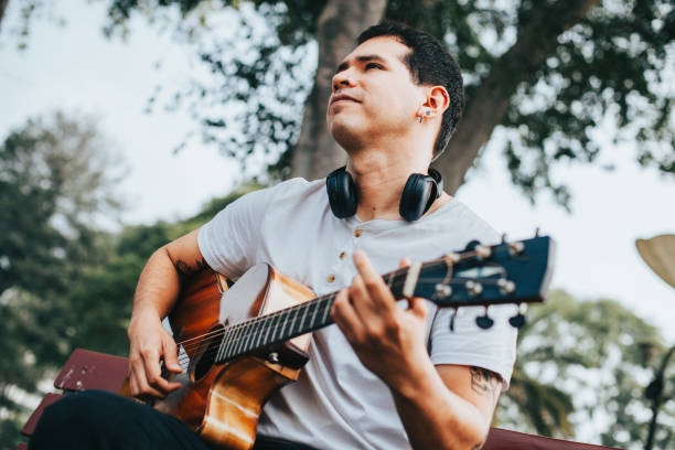 istock Man playing acoustic guitar sitting in a park. 1543043373