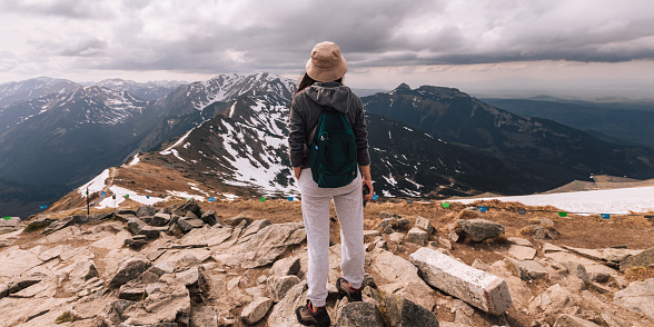 Girl is backpacker with rucksack for touristic equipment, view from the back. Lady is holding mobile phone in the hand. Female portrait of woman, who traveling in mountains. Person doing hiking with warm sportswear outdoors. Lifestyle photography of people, tourism concept.