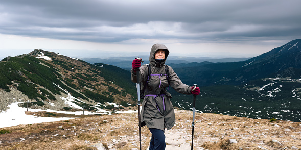 Female portrait of woman, who traveling in mountains. Person doing hiking with warm sportswear outdoors. Lifestyle photography of people and nordic walking, tourism concept.  Girl is backpacker with rucksack for touristic equipment.
