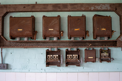 Group of retro rusty electrical isolators and trunking mounted on duck shell blue brick wall.