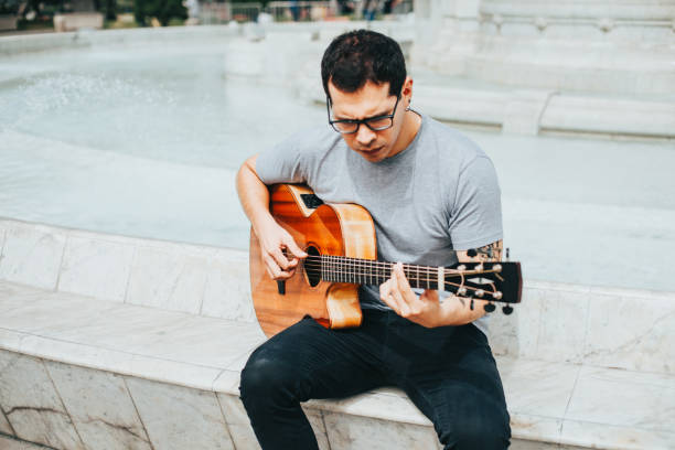 istock Man playing acoustic guitar sitting in a park. 1543054097