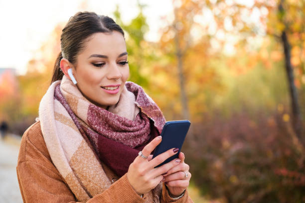 Caucasian woman using the phone wearing earphones smiling in autumn. stock photo