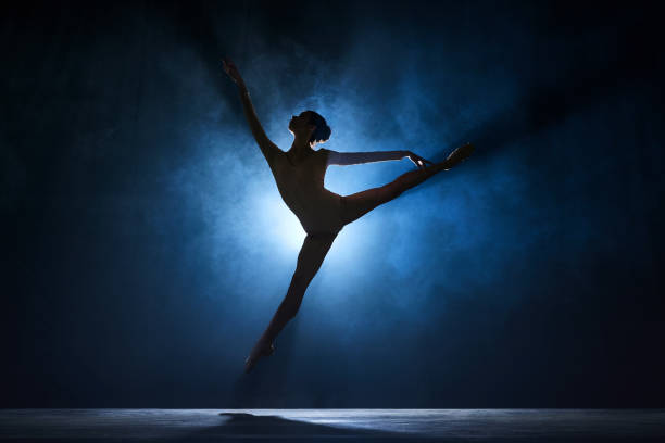 istock Slim, beautiful, graceful ballerina making creative performance on stage against dark blue background with spotlight 1543088866