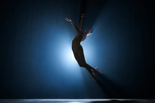 istock Slim, beautiful, graceful ballerina making creative performance on stage against dark blue background with spotlight 1543089081