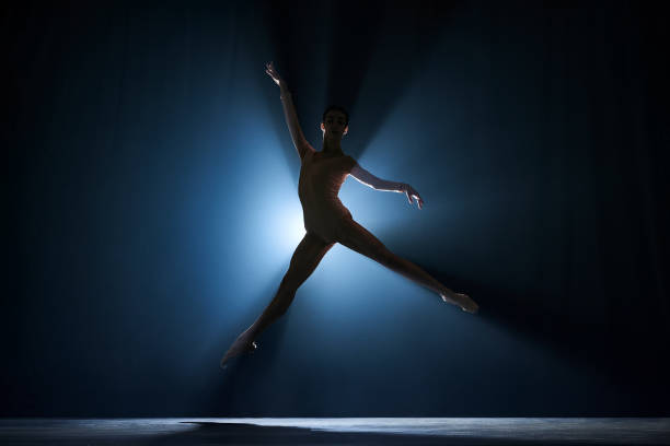 istock Slim, beautiful, graceful ballerina making creative performance on stage against dark blue background with spotlight 1543089090