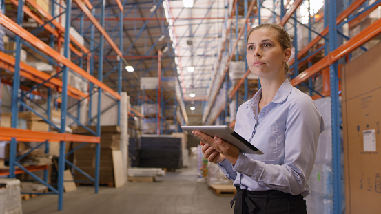 Logistics, digital tablet and woman in warehouse doing stock take or inspection on packages. Technology, factory and young female industrial cargo worker checking cardboard boxes for freight shipping