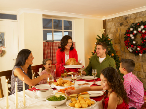 Hispanic family serving Christmas dinner sitting at dining table smiling