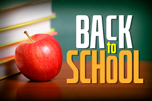 BACK TO SCHOOL lettering on a desk and chalkboard defocused background. Stack of books with an apple on the desk.