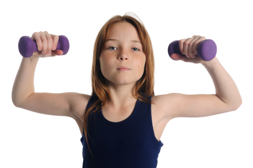 This is a horizontal color photograph of a serious, determined young girl exercising with small, purple hand weights. Shot on white in the studio.