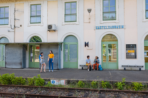 People waiting on a train platform to go to their next destination in Toulouse, France. There are two pairs of friends and they are bonding while they wait for their trains.