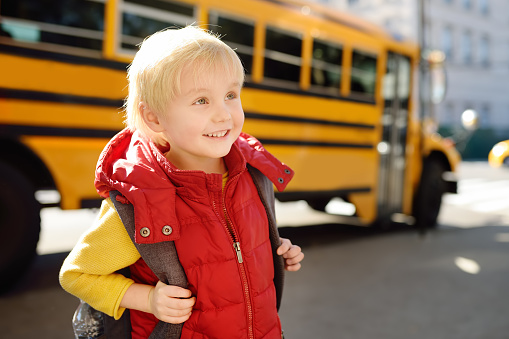 Cute elementary student with schoolbag on background of usa yellow school bus. Back to school.