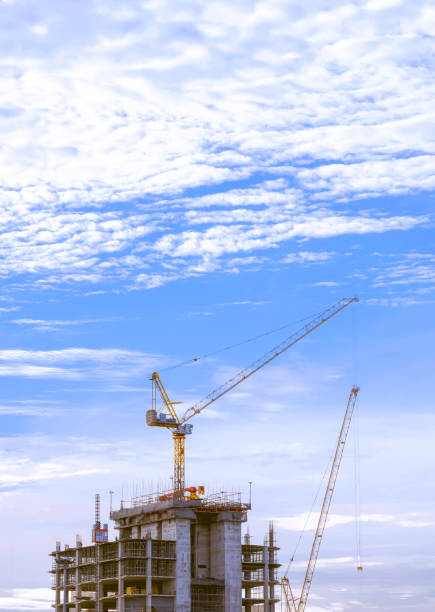Tower cranes are working on top of high building structure against white clouds on blue sky in minimal style and vertical frame