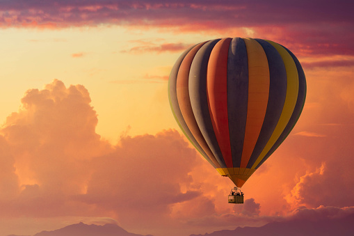 A hot air balloon rising under partly cloudy skies during a brillant sunset with lots of color.