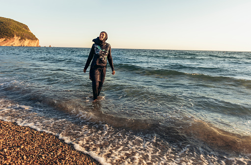 A woman in hijab standing on the beach looking at the horizon