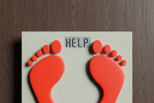 piedi rossi su una bilancia digitale che mostra l'alfabeto help sul suo display. illustrazione del concetto di obesità e problemi di sovrappeso - emaciated weight scale dieting overweight foto e immagini stock