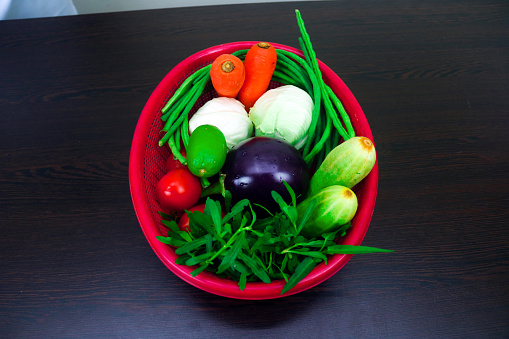 The Colorful and Healthy vegetables include carrots, cabbage, eggplant, cabbage, lemon, tomato, cucumber and collard greens. The vegetables are all arranged in a pleasing manner on the bowl.