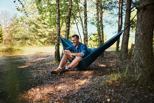 Man in forest sitting on hammock using mobile phone