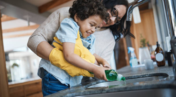 istock Washing, dishes and mother with child in kitchen for learning housework, teaching and helping with chores. Housekeeping, happy family and mom and boy with soap for cleaning, hygiene and development 1543352636