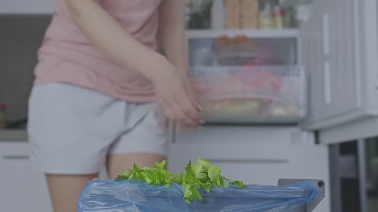 Housewife throws lettuce from fridge compartment into bin