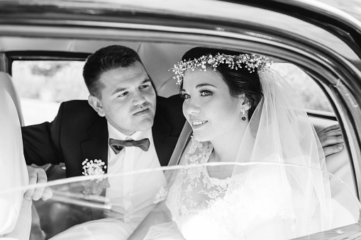 newlyweds in festive clothes sit in a car and look at each other on black and white photography