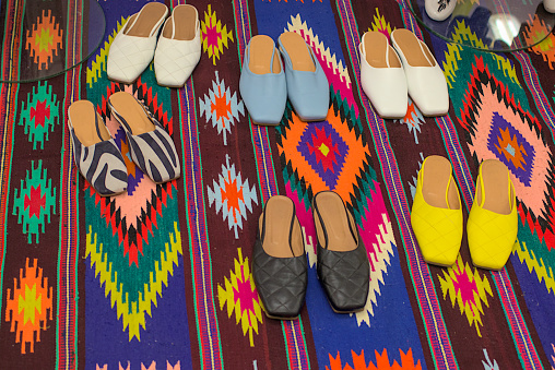 Women's light shoes of various colors are located on a woven carpet with a national Ukrainian pattern. Sale of seasonal shoes in the street market. Style, elegance and fashion.