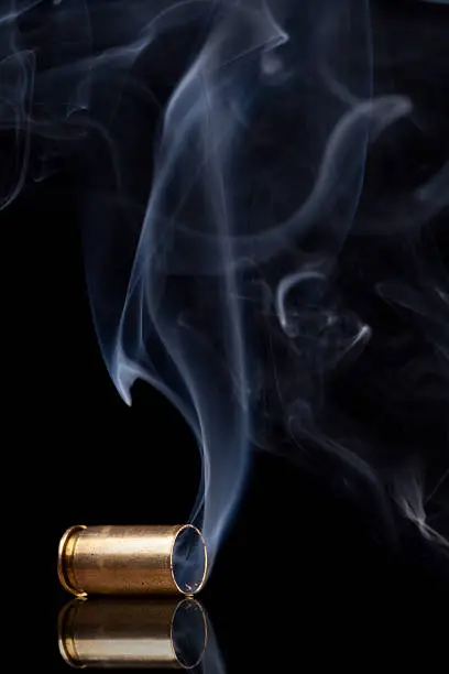 Smoking 9mm bullet casing over black background