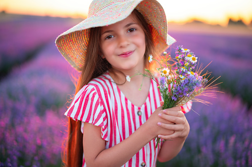 Beautiful woman with dress and hat enjoying color lavender rows in endless blooming field. Girl with flower bouquet