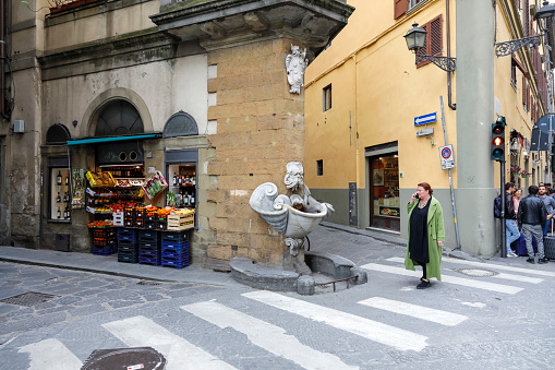 Florence, Italy - April 17, 2023: An old stone fountain located on the corner of a building between two narrow streets in the old town