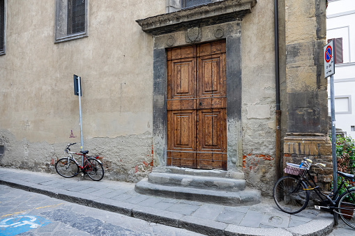 Florence, Italy - April 17, 2023: A massive wooden door to a large brick building. Two bicycles were parked against the wall of the building