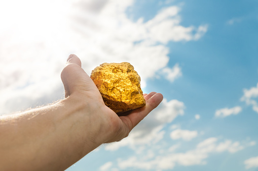 Gold nugget in a man's hand raised to the sky. The concept of wealth and success in the financial sector. Treasure, investment. Mining industry.