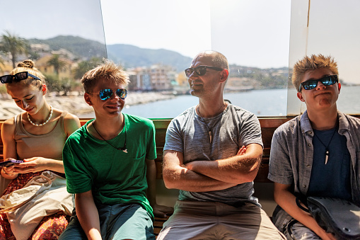 Family waiting for the ferry boat to depart. Father and his teenage kids are sitting by the window. Rapallo, Liguria, Italy.\nShot With Canon R5