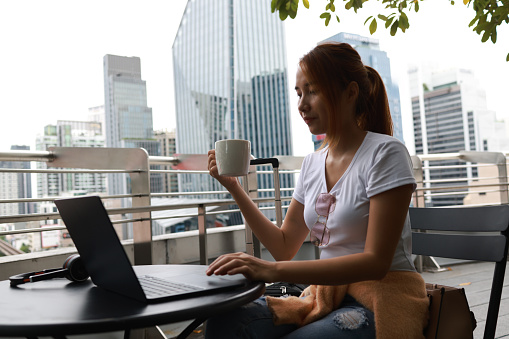Portrait with Young Millennials Asian woman in the city working with a laptop and enjoying a hot drink. Everywhere is a working concept