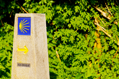 Camino de Santigo milestone, information and directional sign camino del norte, Sobrado, A Coruña province,  Galicia, Spain. Scallop tile, pilgrimage symbol and yellow arrow . Copy space on the right.