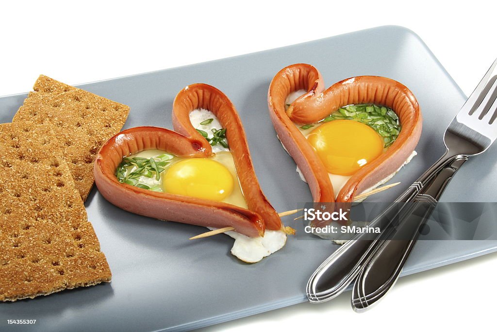 Breakfast on February 14. Two sausages in a heart-shaped fried eggs with green onions. Application Form Stock Photo