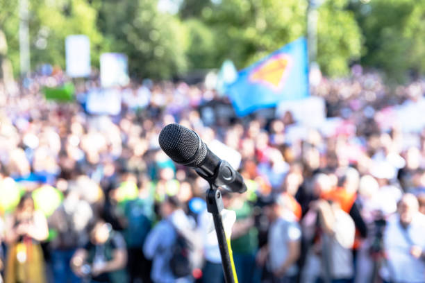 istock Public communication concept. Microphone in focus at mass protest or public demonstration, blurred crowd of people in the background. 1543556192