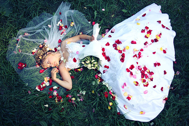 Bride lying on the grass and rose petals stock photo