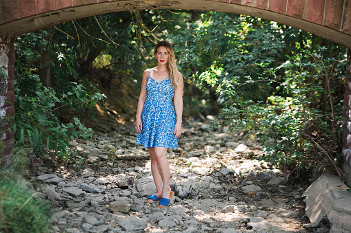 a young pretty woman with a blue dress under a bridge arch in the nature