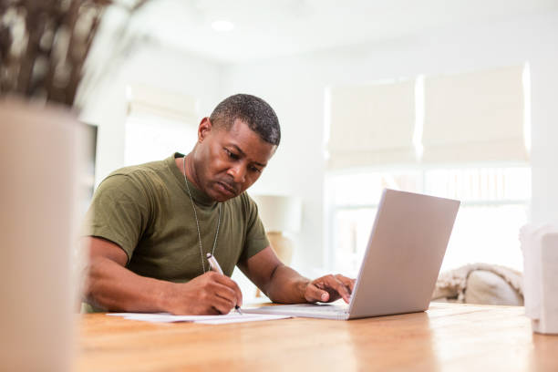 Serious mature soldier continues education online Working at home, the serious mature adult soldier takes continuing education courses online using his laptop. war veteran stock pictures, royalty-free photos & images