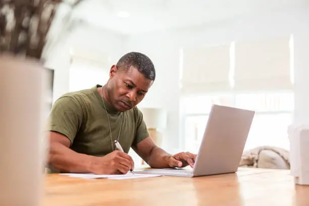 Working at home, the serious mature adult soldier takes continuing education courses online using his laptop.