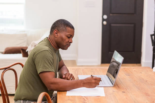istock Using laptop, mature male soldier works on home budget 1543680499