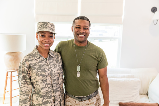 The mid adult female army soldier poses for a photo with her mature adult soldier father.