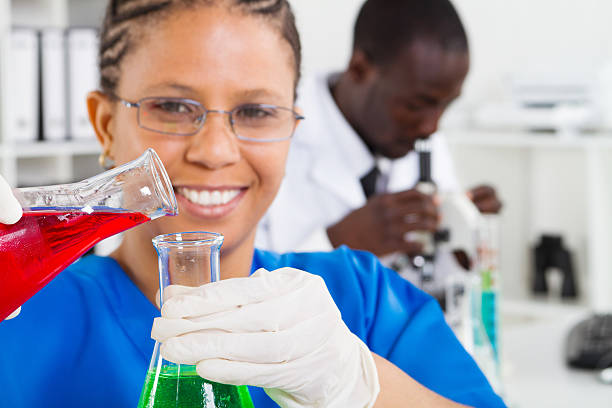 african american female scientist doing experiment african american female scientist doing experiment in lab, background is her colleague working on microscope african american scientist stock pictures, royalty-free photos & images