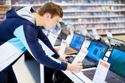 Young man in consumer electronic store checking the configuration in latest laptop computers