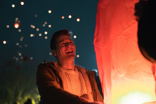istock Excited young man laughing while lighting up a paper sky lantern at event at night 1543719875