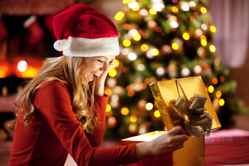 Beautiful blonde young woman wearing Santa's hat is opening Christmas presents.
