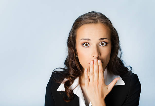 Young businesswoman with wide eyes and hand over mouth stock photo