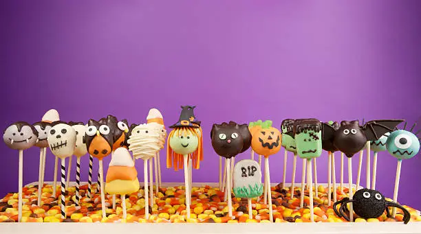 Variety of Halloween mini cakes on sticks against purple background